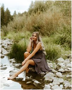 a beautiful woman sitting on top of a rock next to a river