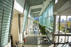 people are walking around in the lobby of an office building with glass walls and large windows