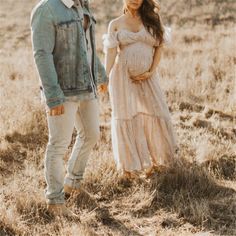 a pregnant woman standing next to a man wearing a denim jacket and dress in a field