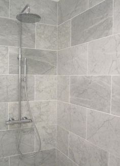 the shower head is mounted to the side of the wall, and it's tiled in gray