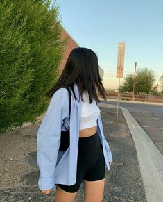 a woman in black shorts and a white shirt is walking down the street with her back to the camera