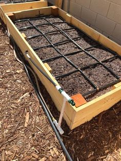 a wooden bed frame sitting on top of mulch next to a brick wall