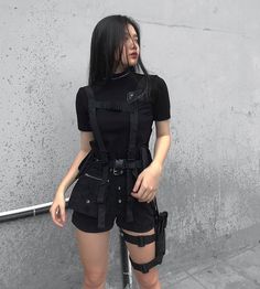 a woman in short shorts and suspenders standing against a wall