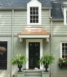 a gray house with black shutters and two potted plants on the front porch