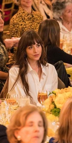 a woman sitting at a table with wine glasses in front of her and other people