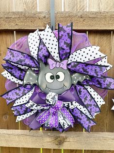 a purple and white wreath with an owl on it's face, hanging from a wooden fence