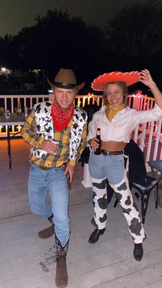 two people dressed in costumes standing on a deck with lights behind them and one holding a beer