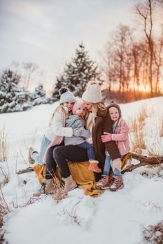 a group of women sitting on top of a log in the snow with their arms around each other