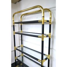 a black and gold metal shelf with three shelves on each side, in front of a white wall