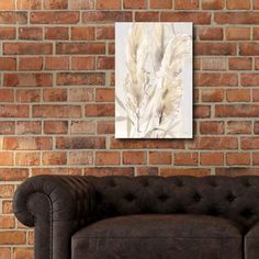 a brown couch sitting in front of a brick wall with a painting hanging on it