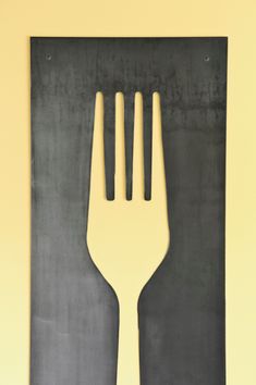 a fork that is sitting on top of a piece of black paper in front of a yellow wall