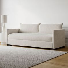 a white couch sitting on top of a wooden floor next to a lamp and rug