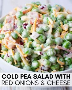 a white bowl filled with peas and cheese on top of a wooden table next to a fork