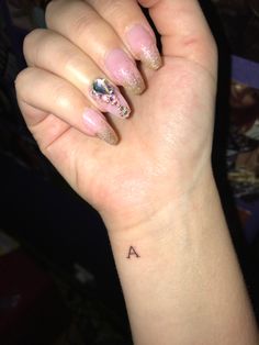 a woman's hand with a small tattoo on her left wrist and pink nails