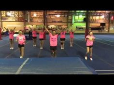 a group of girls in pink shirts standing on top of a blue mat with their hands up