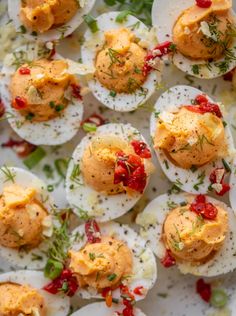 deviled eggs with red peppers and herbs on a white platter, ready to be eaten