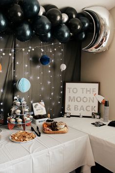 a table topped with lots of desserts next to black and white balloons in the air