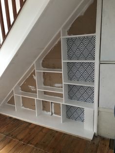 an empty room with some shelves under the stairs and wood flooring in front of it