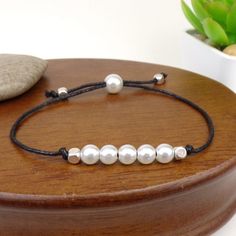 a bracelet with five pearls is sitting on top of a wooden stand next to a potted plant