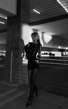 black and white photograph of a woman standing in an empty parking garage with her legs crossed