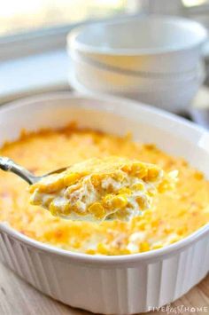 a spoon full of cheesy corn casserole on top of a table