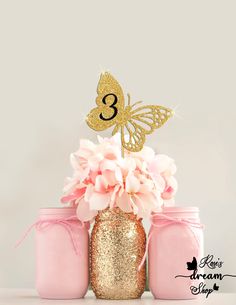 three mason jars with pink and gold flowers in them, one has a butterfly on top