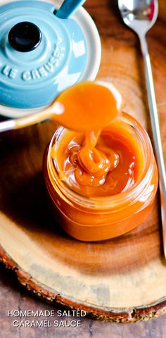 an orange sauce is being poured into a jar on a wooden tray with spoons