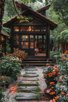 a small house in the middle of some trees and flowers with orange flowers around it