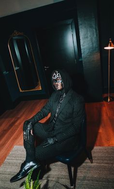 a man sitting on top of a chair wearing a suit and headgear in a dark room