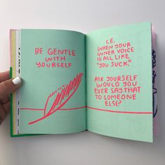 a hand holding an open book with pink writing on it and someone's thumb in the middle