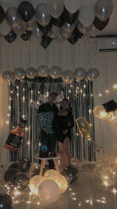 two people standing in front of balloons and streamers on the wall with lights all around them