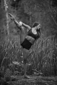 a woman is doing yoga in front of some tall grass and trees with her legs spread out