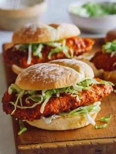 three sandwiches with lettuce and tomato sauce on a cutting board next to some bread