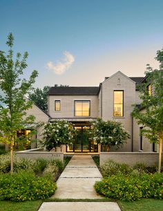 a large house with trees and bushes in front of the entrance to the home at dusk