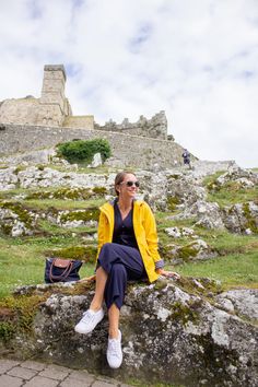 a woman sitting on top of a stone wall next to a grass covered field with a castle in the background