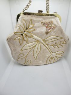 a white purse with gold embroidered flowers and leaves on the front, hanging from a chain