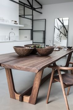 a wooden table with two bowls on top of it and chairs at the base in front of it