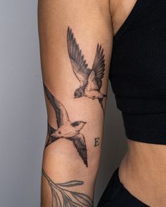 a woman's arm with two birds and the letter e tattooed on her left arm