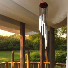 a wind chime hanging from the side of a wooden porch with grass and trees in the background