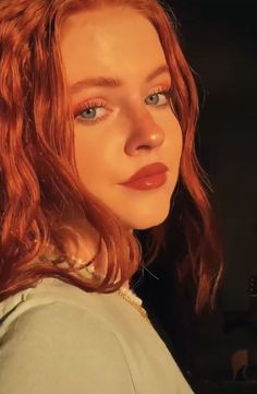 a woman with red hair and blue eyes is looking at the camera while wearing a sweater