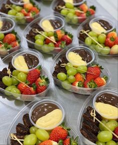 many desserts are arranged in plastic containers on a silver tablecloth with strawberries, grapes and chocolate