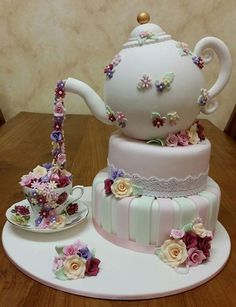 a three tiered cake with flowers on it and a tea pot sitting next to it