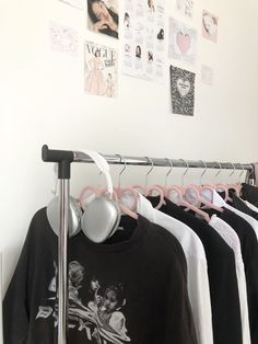 several shirts hanging on clothes racks in front of a white wall with pictures and posters