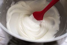 a red spoon in a metal bowl filled with white cream