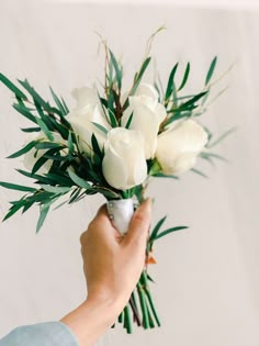 a person holding a vase with white roses in it and greenery on the side