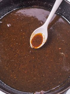 a spoon with some sauce in it on top of a pot filled with liquid and seasonings