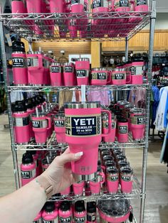 a person holding a pink yeti cup in front of a rack full of bottles