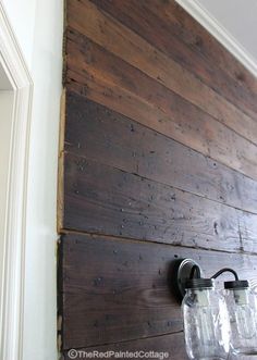 two mason jars are hanging on the wall next to a light fixture that is made out of wood planks