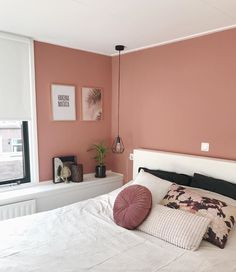 a bedroom with pink walls, white bedding and decorative pillows on the headboard