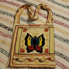 an embroidered bag with a butterfly on it sitting on a striped cloth covered tablecloth